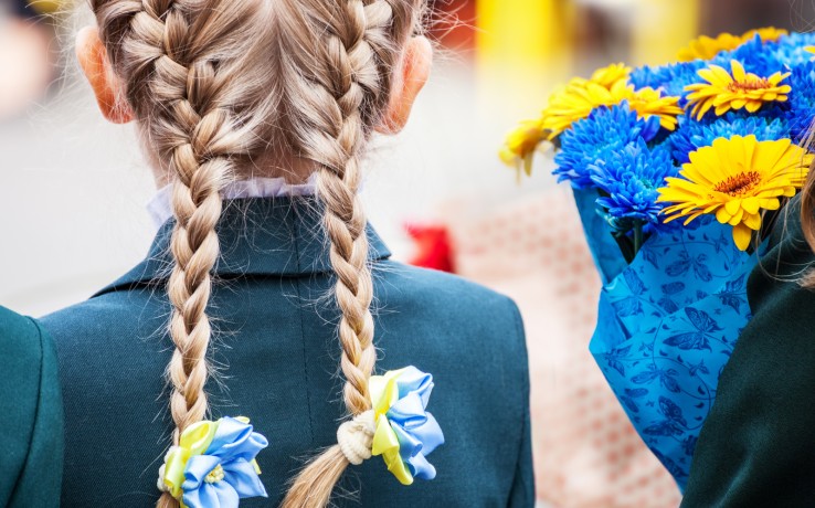 Flicka med blonda flätor och blå skoluniform, bukett med blå och gula blommor syns bredvid.